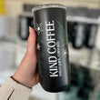 Load image into Gallery viewer, A person's hand holding out a black mug with plants and "KIND COFFEE" written along the side 
